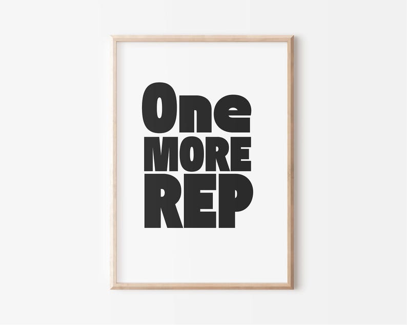 May include: A framed print with the words "One MORE REP" in bold, black letters. The text is centered on a white background, and the frame is a light wood color. The print is a motivational piece.