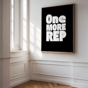 Może przedstawiać: Oprawiony czarno-biały wydruk z napisem "One MORE REP". Grafika jest eksponowana na białej ścianie w pokoju z oknem i drewnianą podłogą.