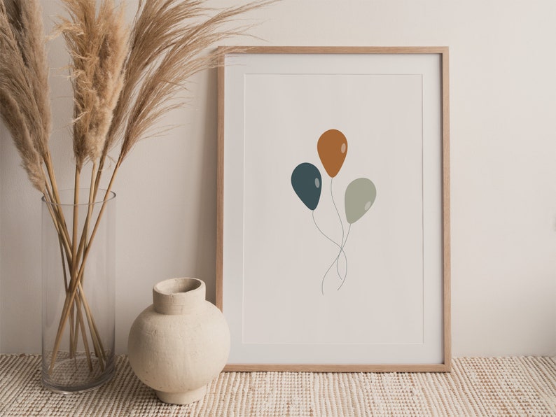 May include: A framed print with a minimalist design featuring three balloons in shades of teal, orange, and gray. The balloons are tied together with a thin string.