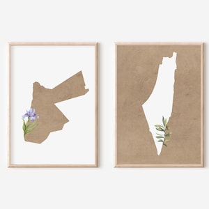 May include: Two framed prints. One features the outline of Jordan in a brown hue, with a purple flower. The other print shows the outline of Palestine in white, set against a brown background, with green leaves.