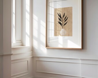 May include: A framed art print featuring a minimalist botanical design. The artwork showcases a black plant with long leaves in a white vase against a tan background. The print is encased in a light brown wooden frame and hangs on a white wall.