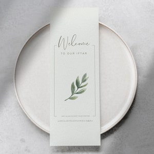 May include: A white card with the text "Welcome to our Iftar" and a green leaf illustration. The card is on a white plate.