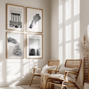 May include: Four framed monochrome prints with the words "LEBANON" and "RAOUCHÉ". The prints show a map, ancient ruins, and a snowy scene. Two wooden chairs with cushions are in front of a window with slatted blinds.