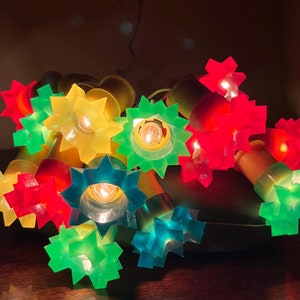 May include: A string of colourful star-shaped Christmas lights with clear bulbs. The lights are red, green, yellow, and blue.