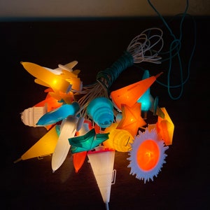 May include: A string of Christmas lights featuring a variety of shapes, including aeroplanes, stars, and a sun. The lights are lit and glowing in a range of colours, including yellow, orange, blue, and green.