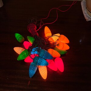May include: A string of Christmas lights featuring a range of colours, including red, green, blue, orange, and yellow. The lights are shaped like pine cones and are connected by a brown wire.