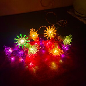 May include: A string of colourful lights with a flower-shaped design. Each light is a different colour, including purple, green, yellow, and red.
