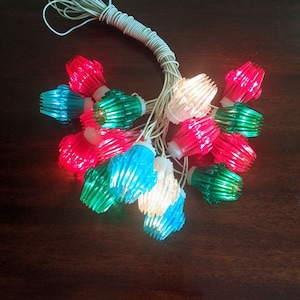 May include: A string of Christmas lights with red, green, blue, and white bulbs. The bulbs are star-shaped and have a textured surface.