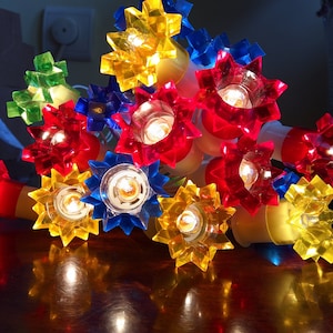 May include: A string of multi-coloured star-shaped Christmas lights. The lights are red, yellow, blue, and green. The lights are lit and glowing.