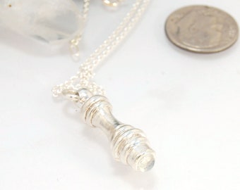 May include: A silver necklace with a pendant that is a small, white, round stone set in a silver casing. The pendant is shaped like a small, round bottle.