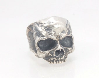 Può includere: Un anello a forma di teschio in argento con un design dettagliato. L'anello è in metallo e presenta un design di teschio realistico.