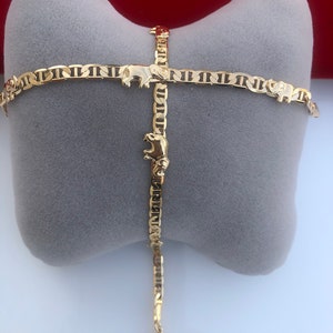 Peut inclure: Un bracelet dor&eacute; avec un motif de breloques &eacute;l&eacute;phants. Le bracelet est compos&eacute; de petits maillons interconnect&eacute;s et est pr&eacute;sent&eacute; sur un coussin gris. Les breloques &eacute;l&eacute;phants sont espac&eacute;es uniform&eacute;ment.