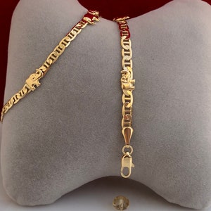 Peut inclure: Bracelet en cha&icirc;ne de couleur or avec un charm en forme d'&eacute;l&eacute;phant. Le bracelet pr&eacute;sente un design de cha&icirc;ne nautique et une fermeture &agrave; fermoir homard. Le charm en forme d'&eacute;l&eacute;phant est visible sur le bracelet. Fond gris et rouge.