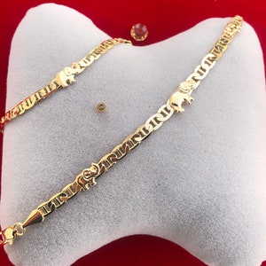 Peut inclure: Un bracelet dor&eacute; avec un charm en forme d'&eacute;l&eacute;phant et un motif de cha&icirc;ne nautique. Le bracelet est pr&eacute;sent&eacute; sur un coussin blanc sur fond rouge. Le bracelet est dot&eacute; d'une fermeture &agrave; fermoir homard.