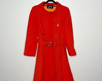 May include: A bright orange double-breasted coat featuring a wide collar, long sleeves, and a matching belt with a gold-toned oval buckle. The coat has four gold-toned buttons on the front and an interior label that reads "Siamie".