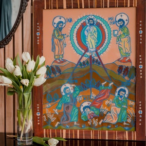 Może przedstawiać: Namalowany obraz w ramie przedstawiający scenę religijną z pięcioma postaciami. Obraz ma brzoskwiniowe tło z niebieskim, czerwonym i białym kolistym wzorem w środku. Postacie są namalowane w stylizowany sposób jaskrawymi kolorami. Obraz jest oprawiony w drewnianą ramę z ozdobną ramką.