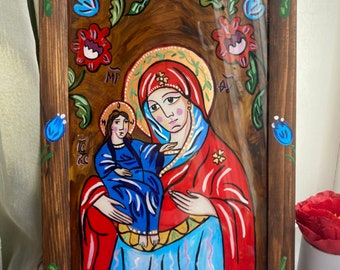 May include: Hand-painted religious icon featuring a woman holding a child, framed in a dark wood. The artwork showcases vibrant colors, with red, blue, and gold accents. Floral patterns adorn the frame, adding a decorative touch to the religious art.