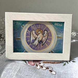 May include: A framed painting depicting a white pelican with open wings, set against a circular background of purple, blue, and gold. The artwork is in a white wooden frame, with the word "Mona" visible.