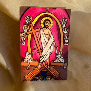 May include: A painting depicting Jesus Christ carrying a cross, surrounded by angels. The painting is done in a vibrant style with bright colors and bold lines.