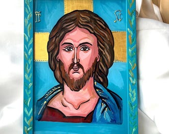 May include: Hand-painted icon of Jesus Christ in a teal frame. The artwork features a central figure with brown hair and beard, wearing a blue robe. The background includes a gold cross and teal accents, with a decorative leaf pattern on the frame.