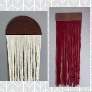 Könnte beinhalten: Zwei Wandbehänge mit Holzaufsätzen und langen Garnsträngen. Der linke Wandbehang hat weißes Garn und der rechte Wandbehang hat rotes Garn.