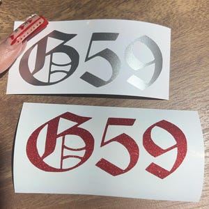 May include: Two versions of a 659 sticker. One is silver and the other is red glitter. Both are in a gothic font.