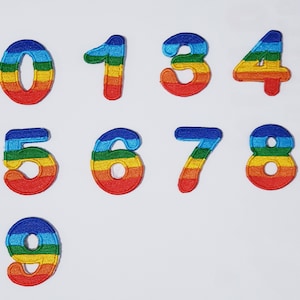 Peut inclure: Patchs en feutre de couleur arc-en-ciel des chiffres 0 à 9. Chaque chiffre est souligné en bleu, puis en rouge, orange, jaune, vert et enfin en bleu.