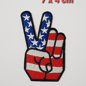Könnte beinhalten: Ein gestickter Bügel-Patch mit einem Peace-Zeichen in Form einer Hand mit dem Design der amerikanischen Flagge. Der Patch ist 7 x 4 cm groß.