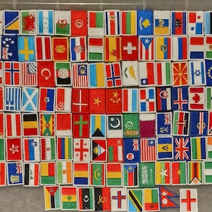 May include: A collection of embroidered fabric patches featuring flags from various countries. The patches are arranged in rows and columns on a white surface.