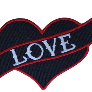 Puede incluir: Parche negro en forma de corazón con borde rojo y una pancarta blanca que dice "LOVE" en una fuente de estilo vintage.
