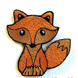 Peut inclure: Un renard brodé marron sur fond blanc. Le renard est assis, la queue enroulée derrière lui. Le renard a des yeux noirs et un nez noir.