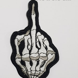 Pode incluir: Um remendo preto bordado com uma mão de esqueleto branca mostrando o dedo do meio. O remendo mede 9,5 x 5,5 cm.