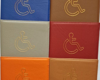 May include: A set of ten different colored leather card holders with a gold wheelchair symbol embossed on the front. The colors include pink, black, blue, brown, gray, red, orange, tan, hot pink, and purple.