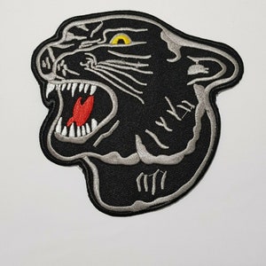 May include: Black and white embroidered iron-on patch of a roaring panther head with a yellow eye and red tongue.