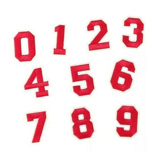 May include: Ten red felt iron-on numbers, 0 through 9, with white outlines. The numbers are arranged in three rows.
