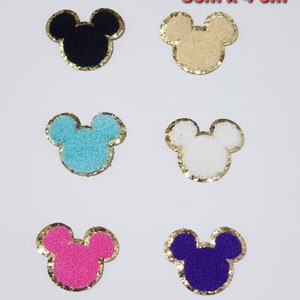 Puede incluir: Seis apliques de Mickey Mouse de pelo con ribete de purpurina dorada. Los apliques son de color negro, beige, azul claro, blanco, rosa y morado.