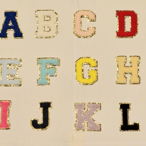May include: A set of felt alphabet letters in various colours, including blue, pink, yellow, red, white, and black. The letters are outlined in gold and are arranged in alphabetical order.