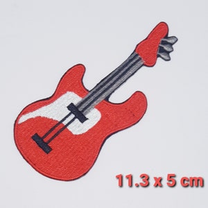 Peut inclure: Guitare électrique rouge avec un pickguard blanc et des cordes noires. La guitare mesure 11,3 cm sur 5 cm.
