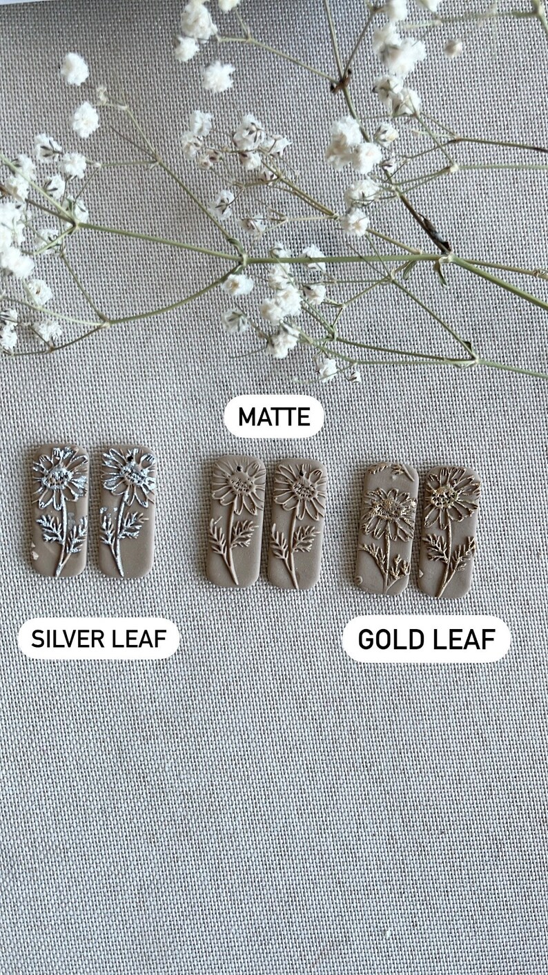 May include: Three pairs of rectangular ceramic earrings with a floral design. The earrings are in three finishes: matte, silver leaf, and gold leaf.