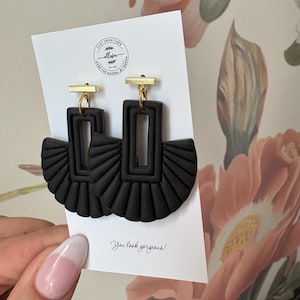 Könnte beinhalten: Schwarze Statement-Ohrringe mit rechteckigem und fächerförmigem Design. Die Ohrringe sind aus mattem, schwarzem Material gefertigt und haben goldfarbene Akzente. Sie werden auf einer weißen Karte mit dem Text "You look gorgeous!" präsentiert.