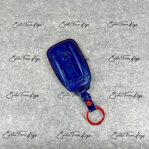 May include: A blue key fob cover with red stitching and a red key ring. The cover has a textured pattern and the Acura logo. The text "Exotic Trim Keys" is repeated across the background.
