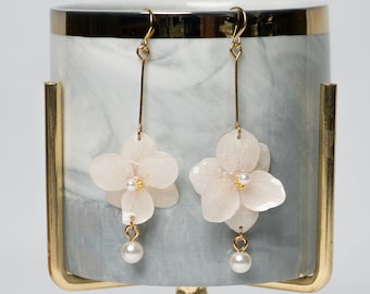 May include: A pair of delicate white flower earrings with pearl accents hanging from a gold stand.