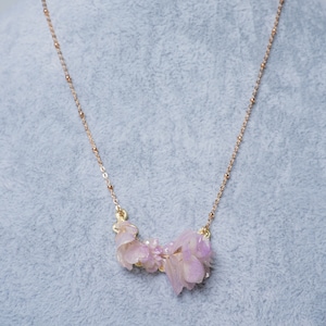 May include: A delicate gold chain necklace with a pink flower pendant. The pendant is made of several layers of petals, giving it a layered and dimensional look.