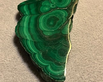 May include: A green malachite stone with a swirling pattern and a gold edge.