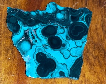 May include: A polished slab of malachite, a vibrant green mineral with swirling patterns of dark green and teal. The stone's surface is smooth, showcasing its natural beauty and unique banding.