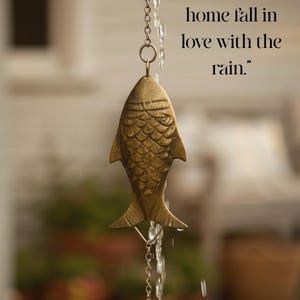May include: A brass fish-shaped wind chime hanging from a chain, with water cascading down. The chime has a textured surface and is suspended in front of a blurred background. Text reads: "Let your home fall in love with the rain."