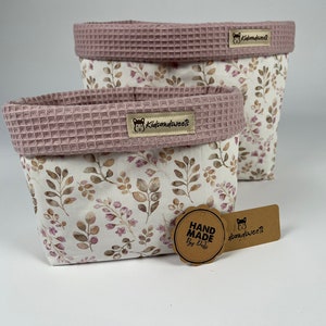 May include: Two pink and white fabric storage baskets with a floral pattern. The baskets have a pink waffle-textured top and a brown label with the text "kidsandweets". A brown tag with the text "HAND MADE by Kati" is in the foreground.