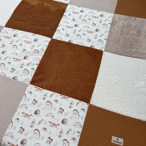 Può includere: Un tappetino da gioco per bambini di colore marrone, bianco e beige con diverse texture. Il tappetino presenta un motivo di volpi, cervi, gufi e altre creature del bosco. Il tappetino è realizzato con materiali morbidi e confortevoli ed è perfetto per i bambini da esplorare e giocare.