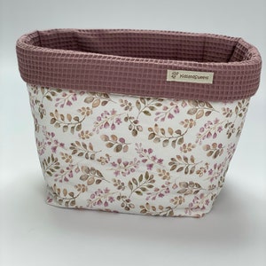 May include: A white fabric storage basket with a pink floral pattern and a pink waffle-textured top. The basket has a label that says "KidsandSweets".