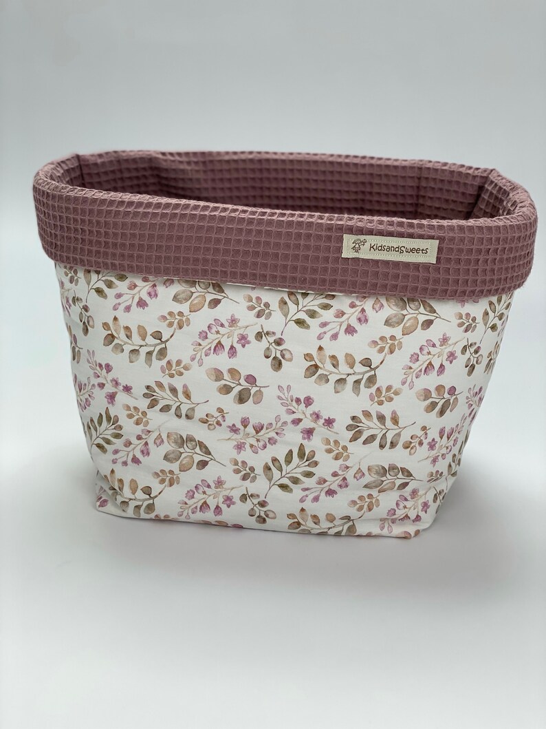 May include: A white fabric storage basket with a pink floral pattern and a pink waffle-textured top. The basket has a label that says "KidsandSweets".